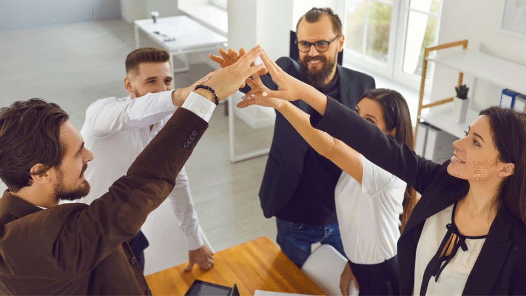 Equipo de trabajo diverso levantando las manos en señal de unión y colaboración dentro de una oficina moderna.