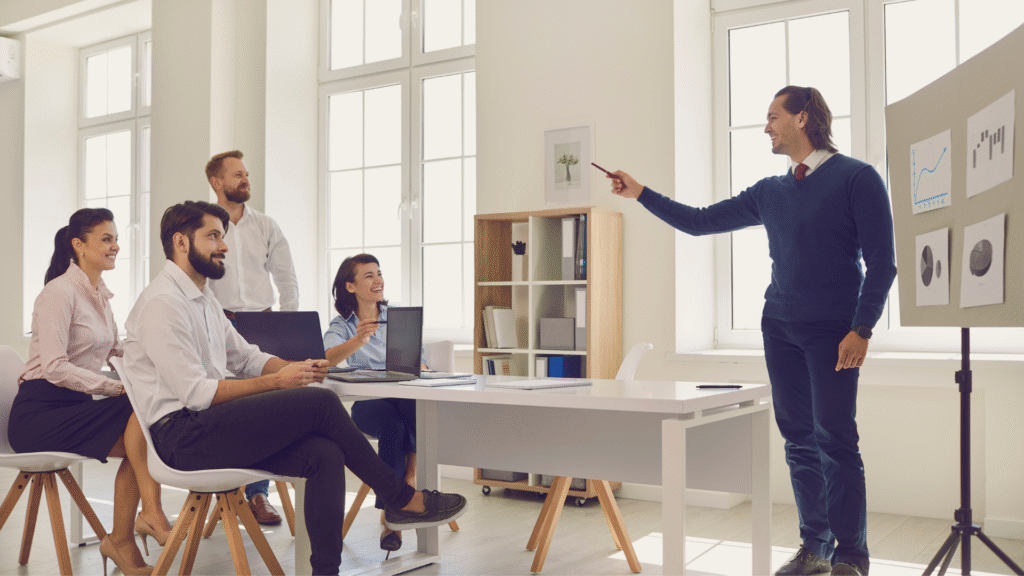 Líder empresarial guiando una reunión frente a su equipo en una oficina iluminada y moderna.
