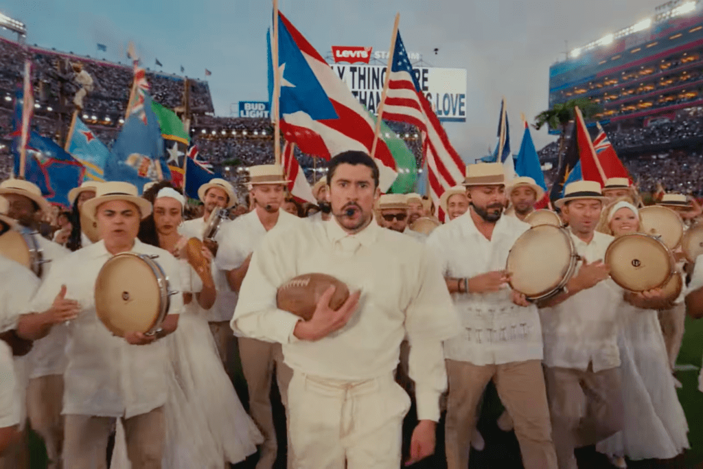 Bad Bunny avanza al frente de un grupo multicultural con banderas de distintos países latinoamericanos durante el medio tiempo del Super Bowl, mientras un mensaje de amor aparece en las pantallas del estadio.